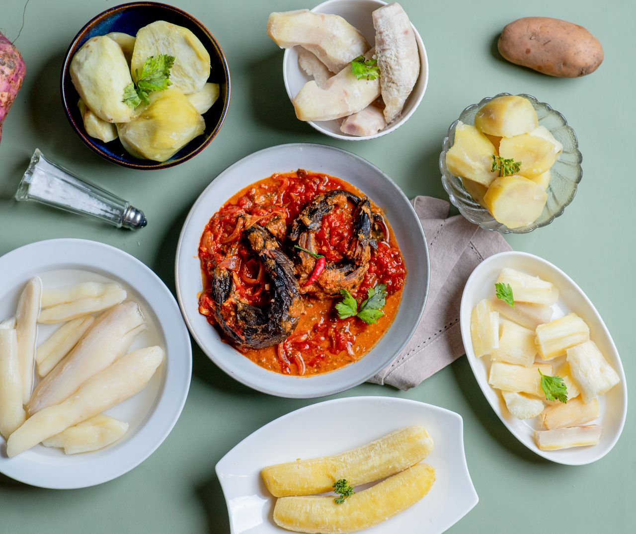 A vibrant display of traditional African dishes featuring banana, cassava, yams, and spicy stewed fish in Burundi.
